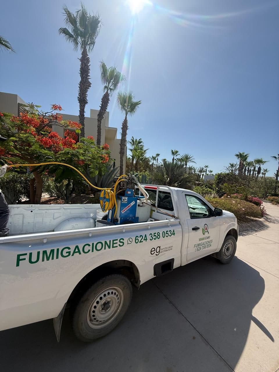 Equipo de aplicación con tanque y manguera montado en la unidad, entre palmeras y flores